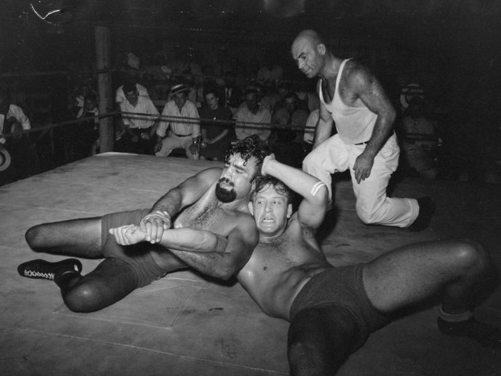 Two wrestlers grapple in an outdoor ring in Sikeston, Missouri, in 1938 while a referee watches