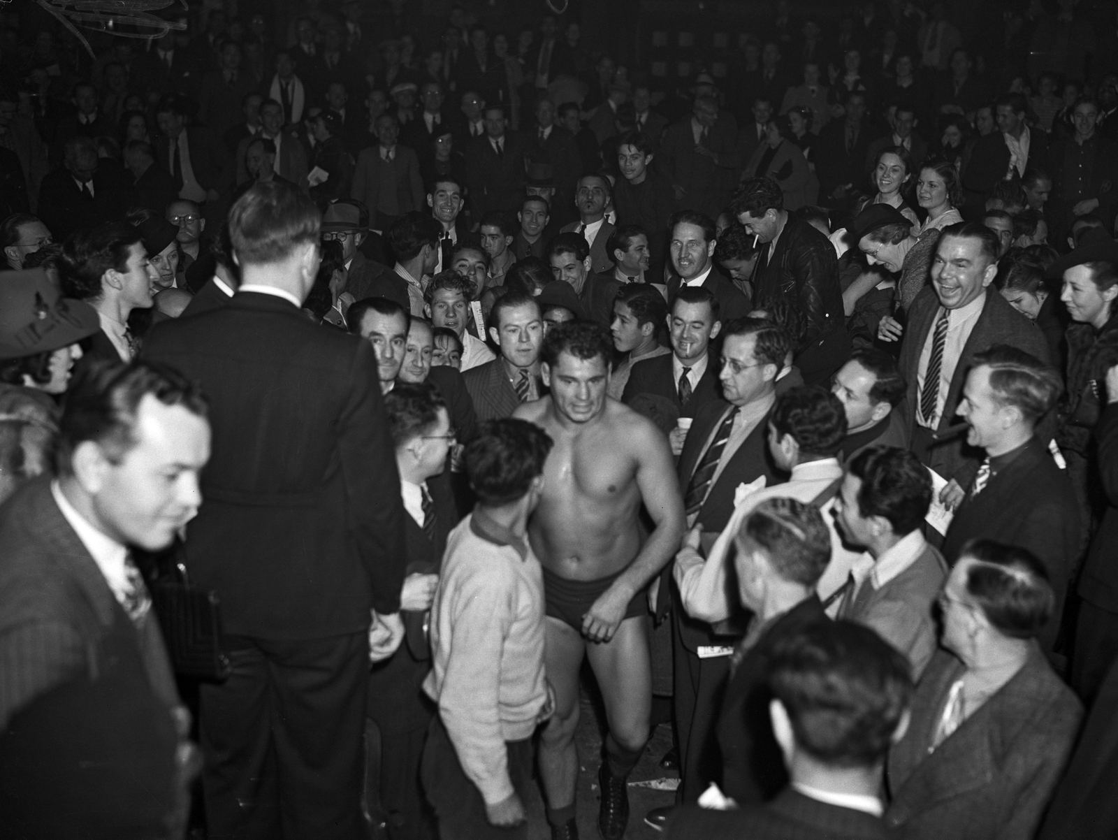 Wrestler Sandor Szabo walking shirtless through a packed crowd toward the ring in the 1930s